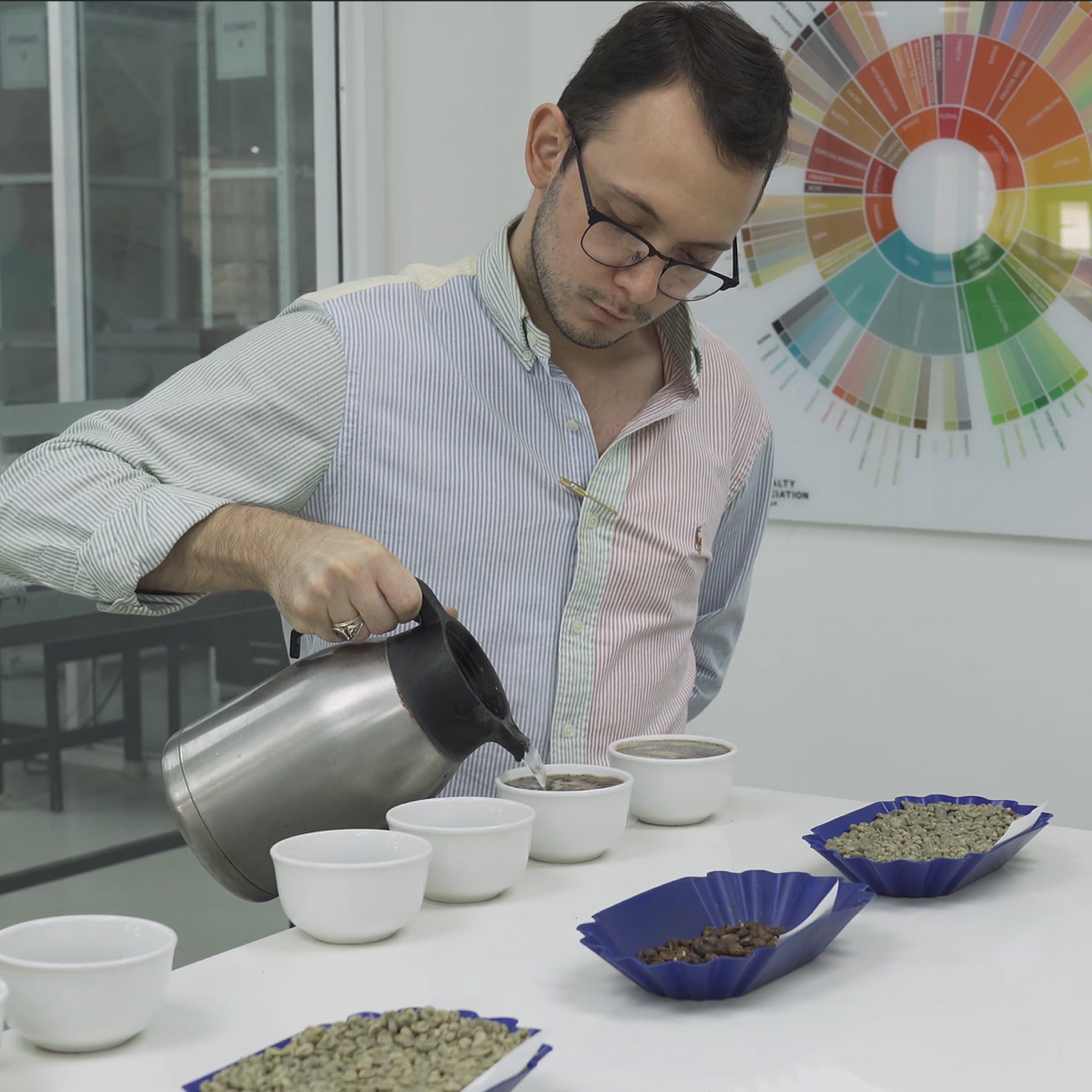 Man pouring coffee into cups with bowls of coffee beans on a table.